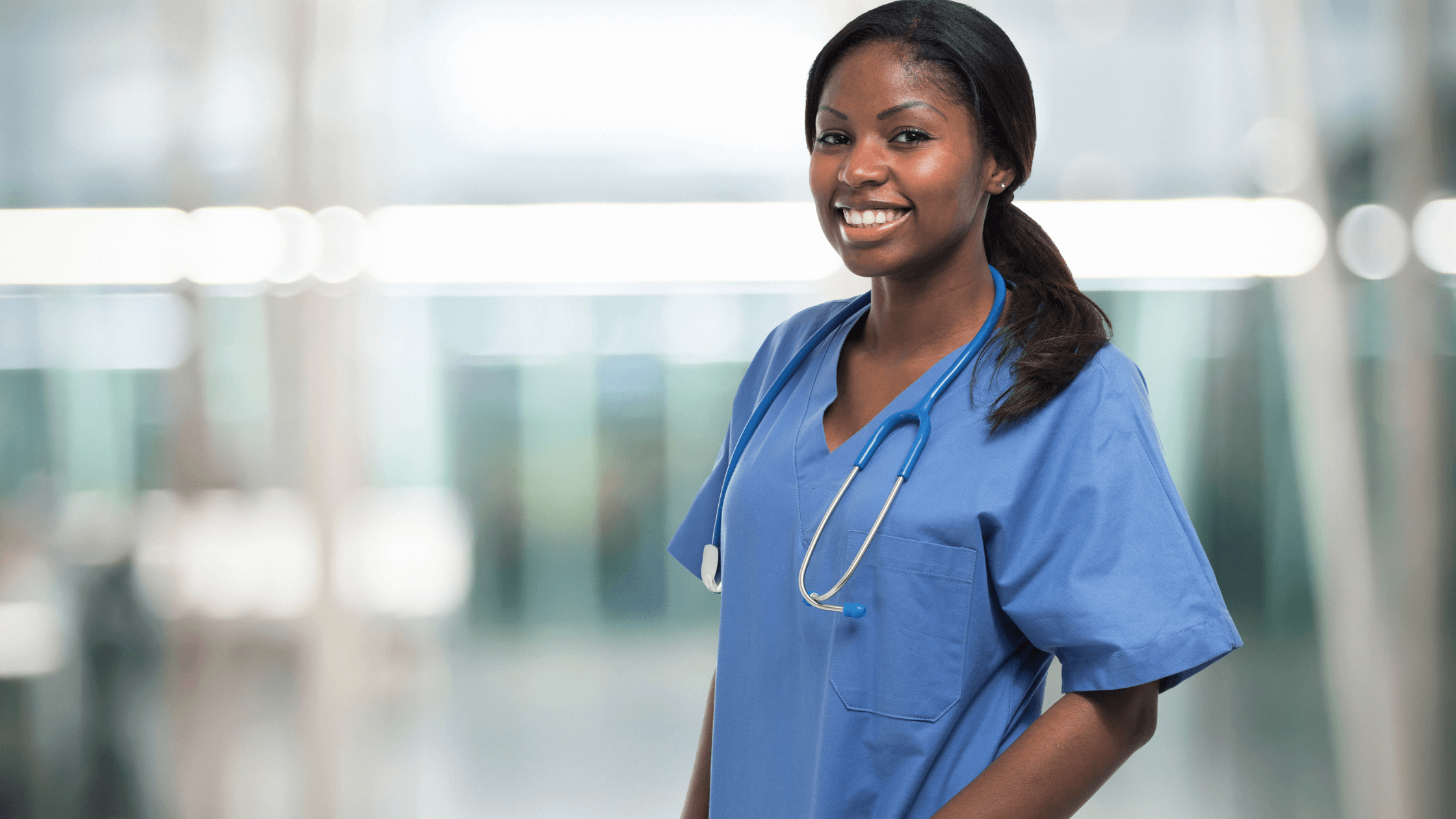 A correctional nurse standing in a hallway in scrubs, smiling.