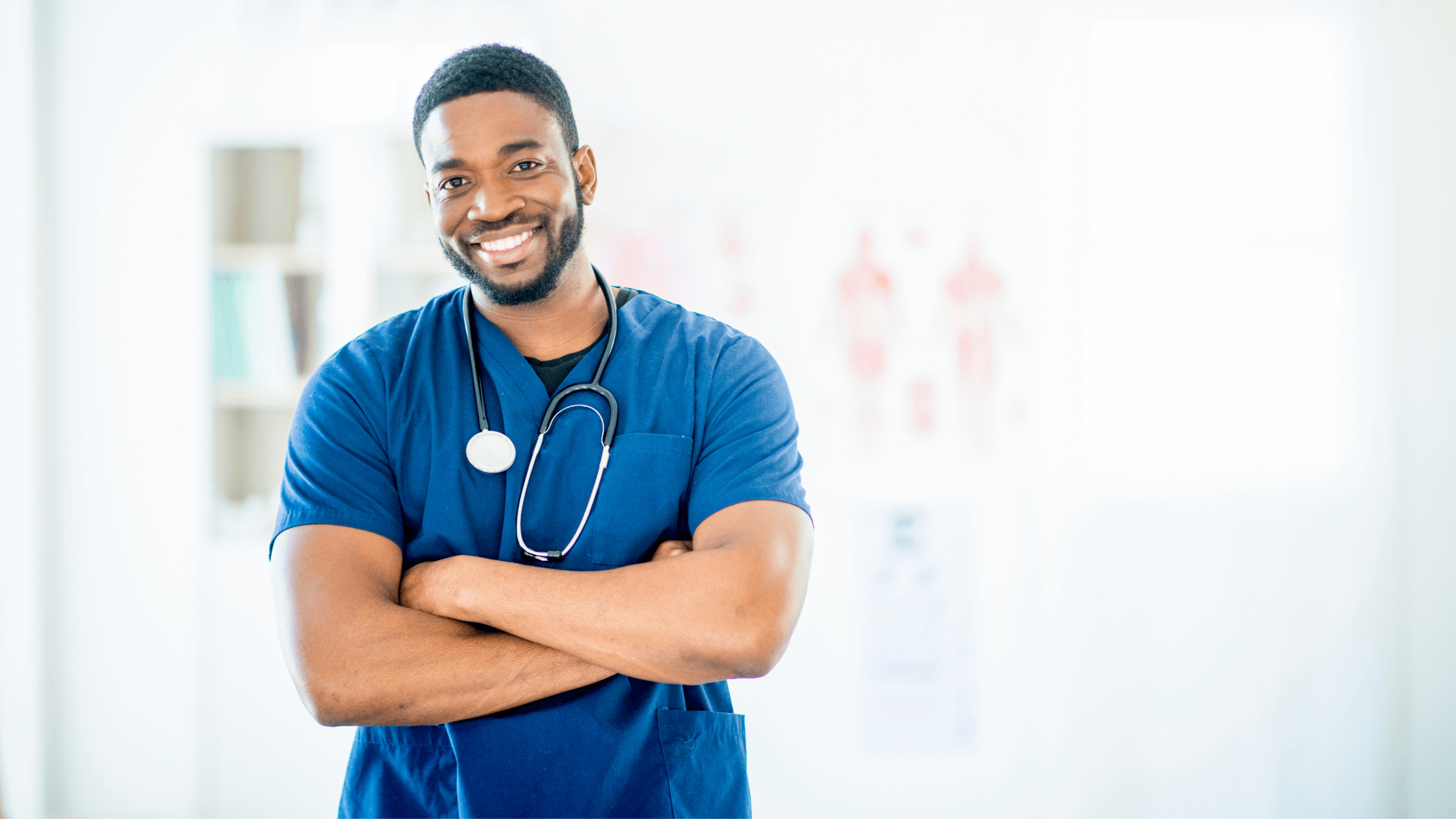 A nurse in scrubs with a stethoscope, standing with his arms crossed.