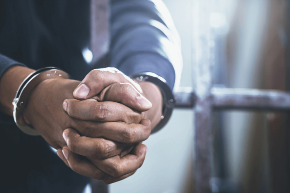 Close-up of a person's hands, handcuffed and behind bars.