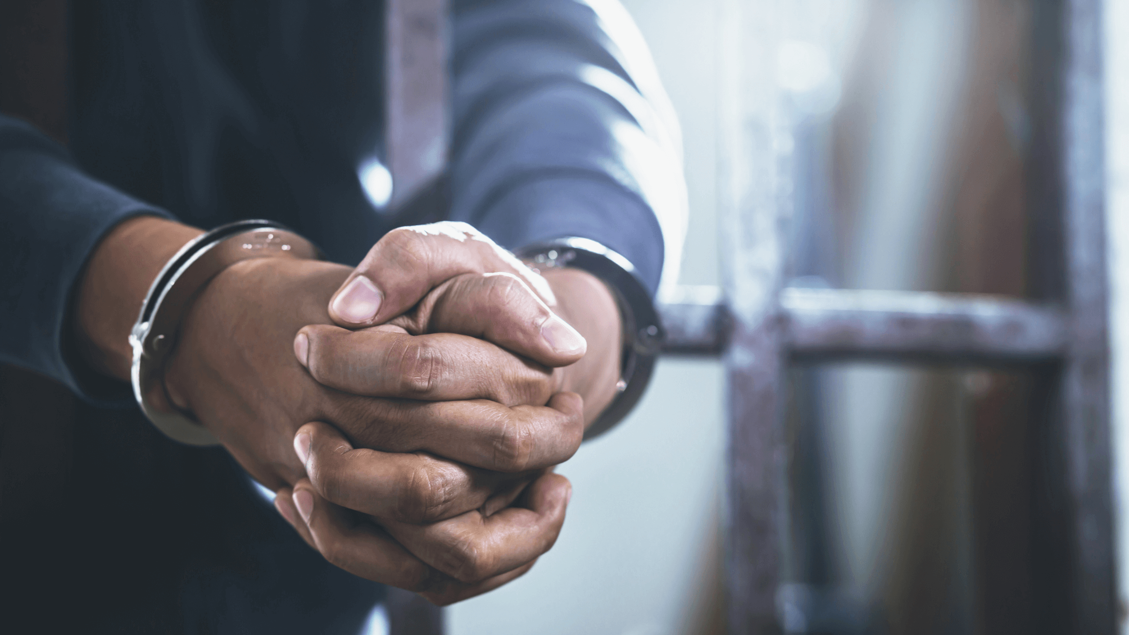 Close-up of a person's hands, handcuffed and behind bars.