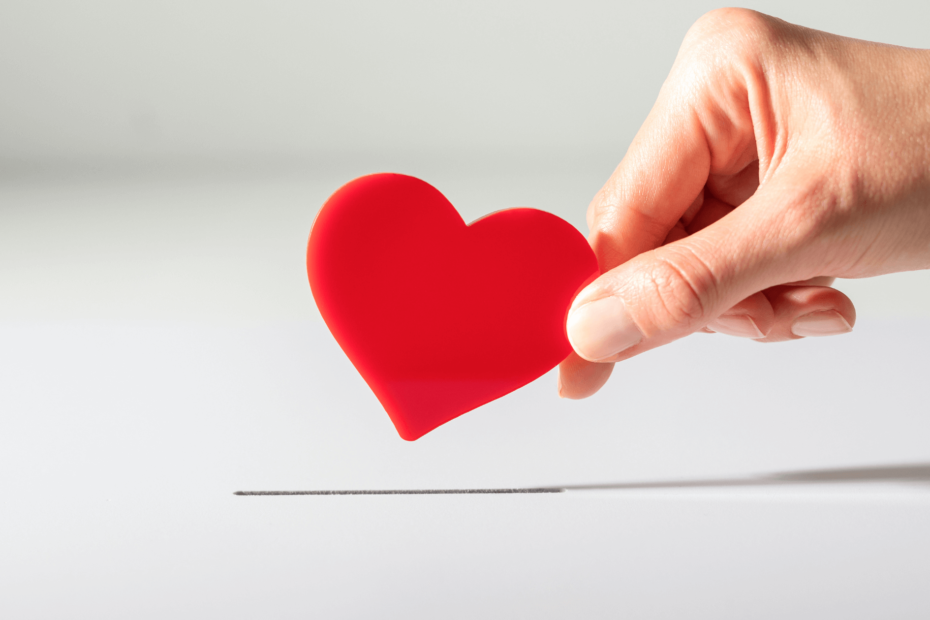 A hand putting a cutout heart into a box, like a donation.