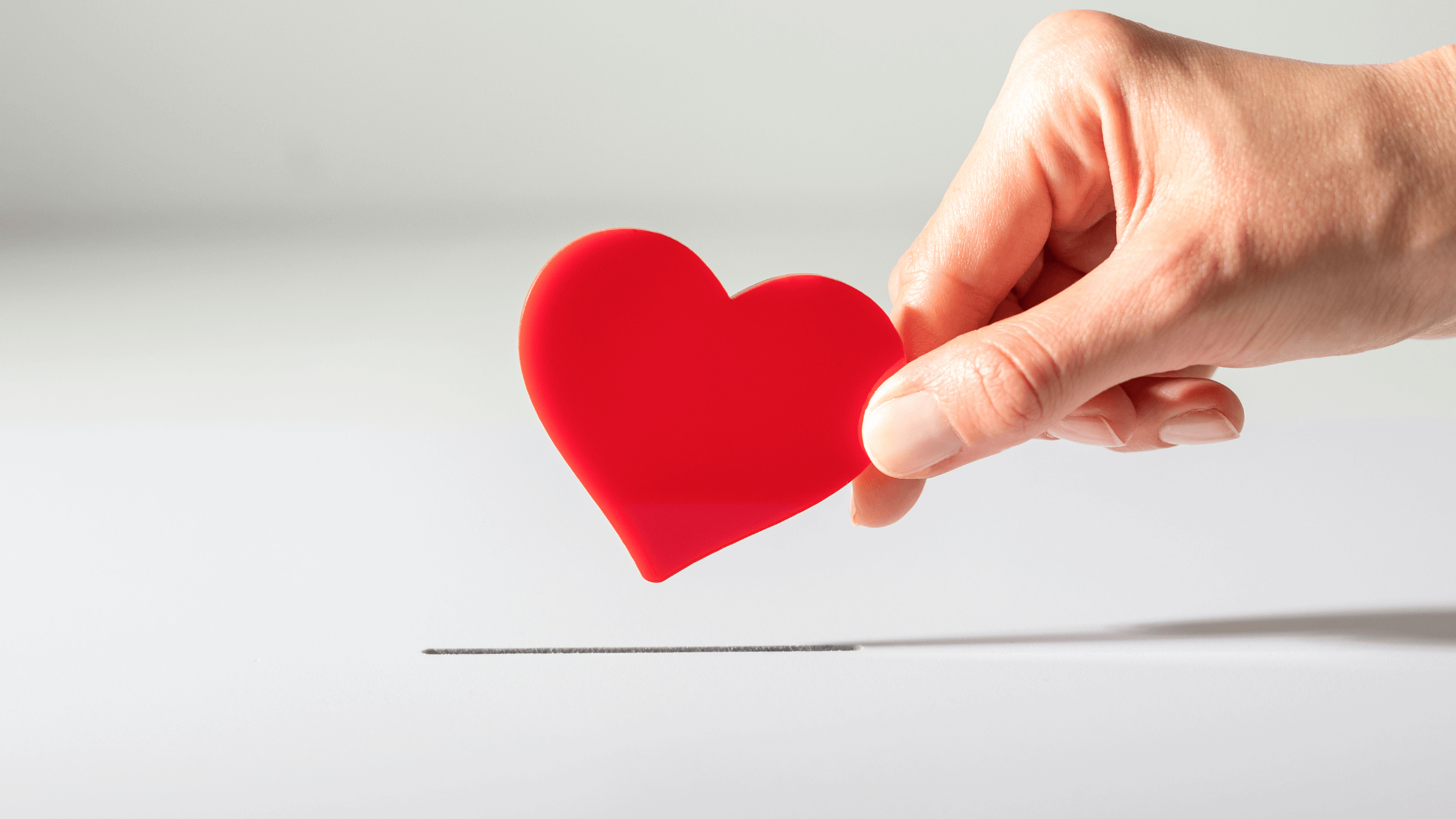 A hand putting a cutout heart into a box, like a donation.
