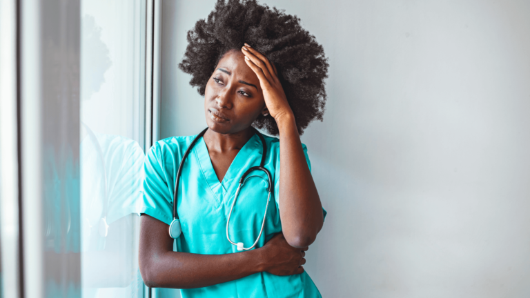 A nurse looking out the window with her head in her hand.