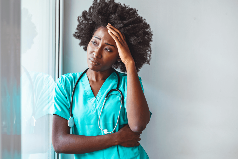 A nurse looking out the window with her head in her hand.