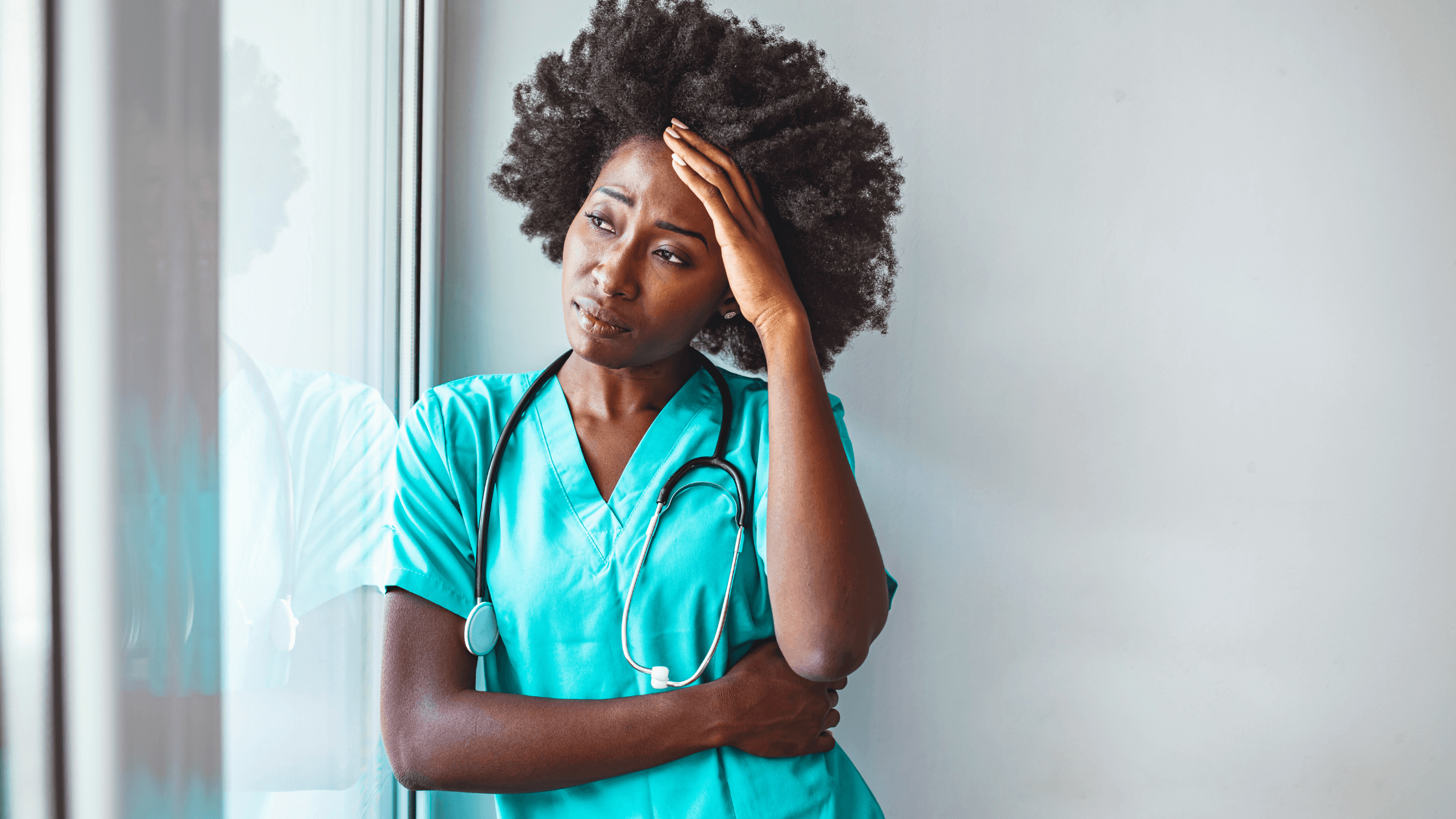 A nurse looking out the window with her head in her hand.