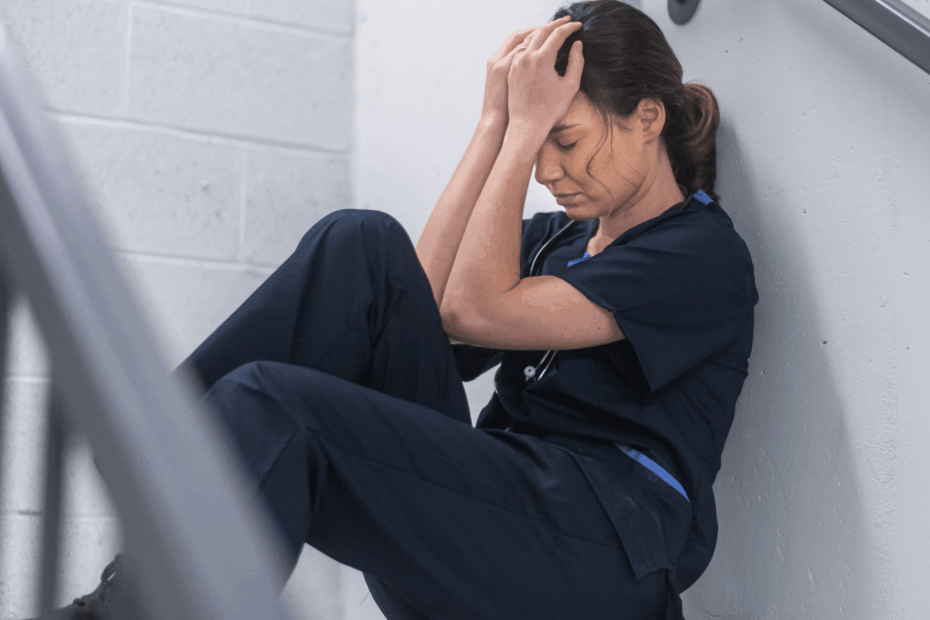 A nurse sitting in a stairwell with her head in her hands.