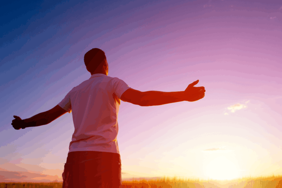 A man standing with his arms outstretched, facing the sunset.