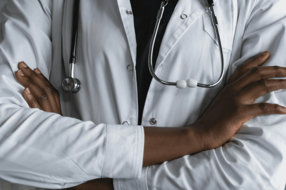 A close up of a man in a white coat with a stethoscope around his neck and his arms crossed in front of him.