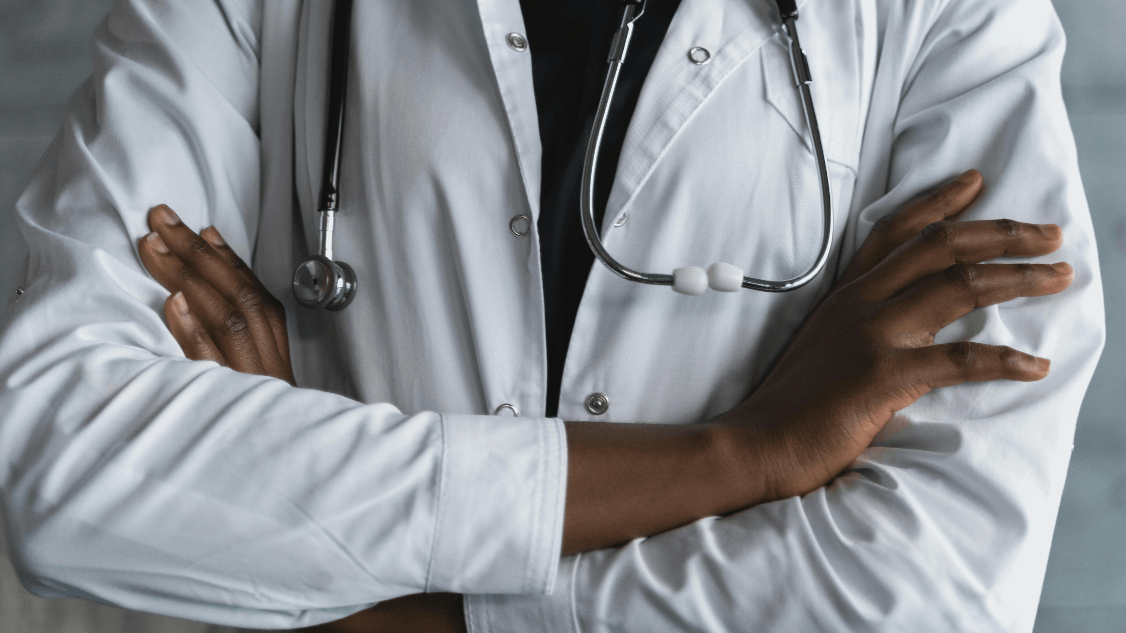 A close up of a man in a white coat with a stethoscope around his neck and his arms crossed in front of him.